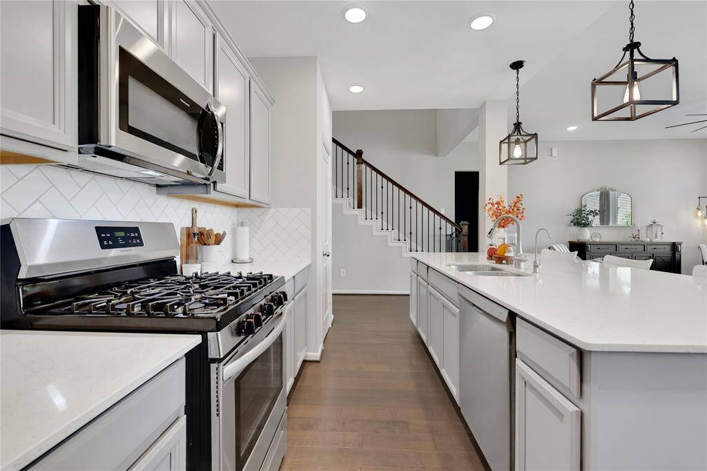 The kitchen features quartz countertops, a gas stove, and an over-the-range microwave. Elegant pendant lights hang above the island, and the space opens to a dining area. Hardwood floors extend throughout, and there's a staircase leading to the upper level.