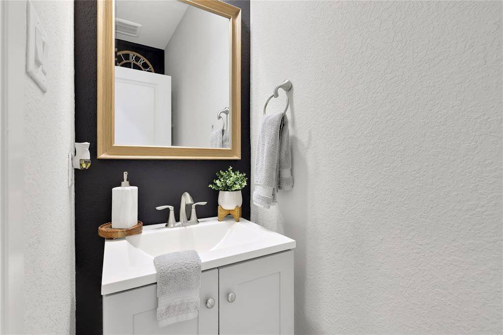The half-bathroom features a clean, white vanity with a dual-handle faucet, a framed mirror, and contrasting dark walls that create a stylish and contemporary look. The space is simple, functional, and elegant