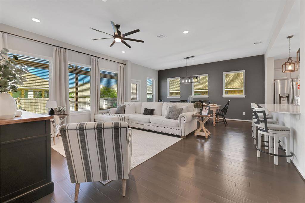 With an open-concept living space and combined living and dining area. The room has elegant hardwood floors, a neutral color palette, and plenty of natural light from large windows..the adjacent breakfast bar offers additional seating. The space is well-lit with a contemporary ceiling fan and stylish pendant lights over the kitchen island.