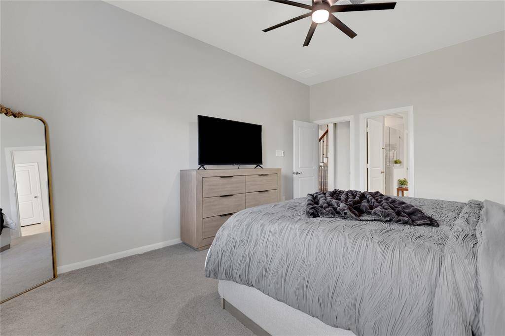 You're looking at a modern bedroom, spacious,  well-lit with a ceiling fan, and has carpeted flooring. It includes double doors leading to the bathroom.