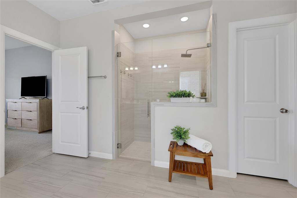 This is a modern, well-lit bathroom featuring a spacious walk-in shower with clear glass doors, and neutral-toned tile walls.