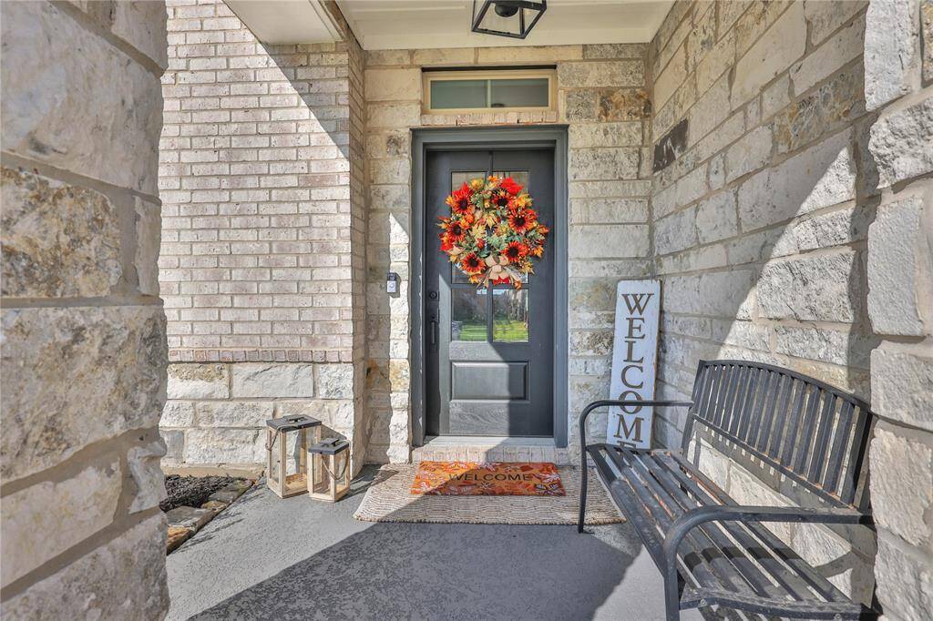 This is a welcoming front entryway featuring a sturdy stone facade, a dark-colored front door adorned with a vibrant wreath, a "Welcome" sign, and a comfortable bench to enjoy the neighborhood views.