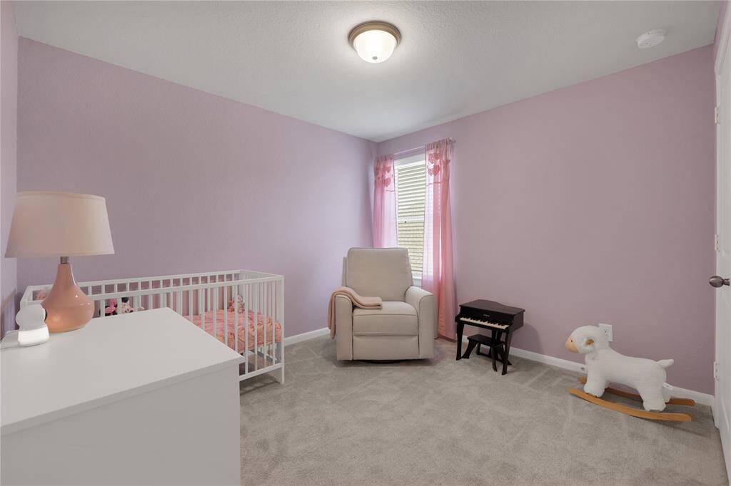This is a cozy, well-lit nursery room featuring soft purple walls and plush carpeting. playful accents  Perfect for a family.