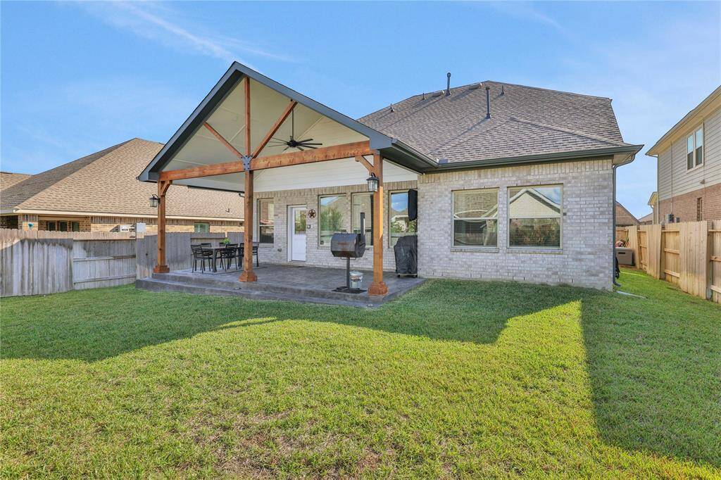 The well-maintained backyard features a spacious covered patio with a ceiling fan, perfect for outdoor dining and relaxation, complemented by a lush green lawn enclosed by a privacy fence.