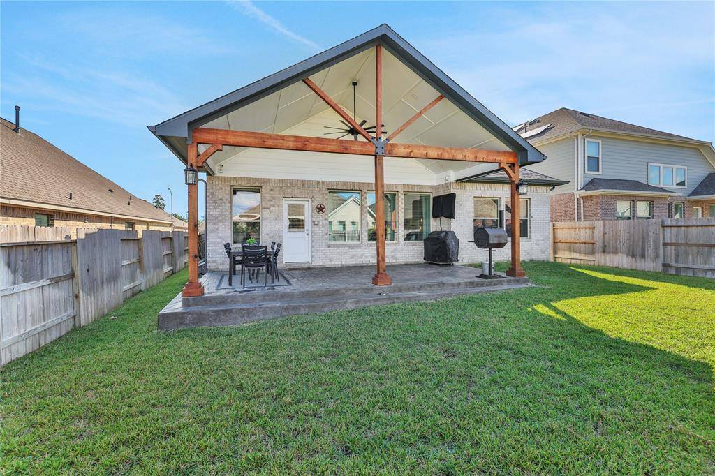 This photo showcases a spacious backyard with a large covered patio featuring a modern design, perfect for outdoor dining and entertaining. The yard is well-maintained with green grass and enclosed by a wooden privacy fence.