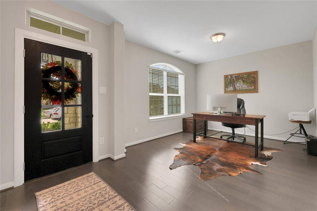 This is a well-lit home office space, dark hardwood floors complement the neutral walls. The room has a welcoming feel with natural light coming in from the window.