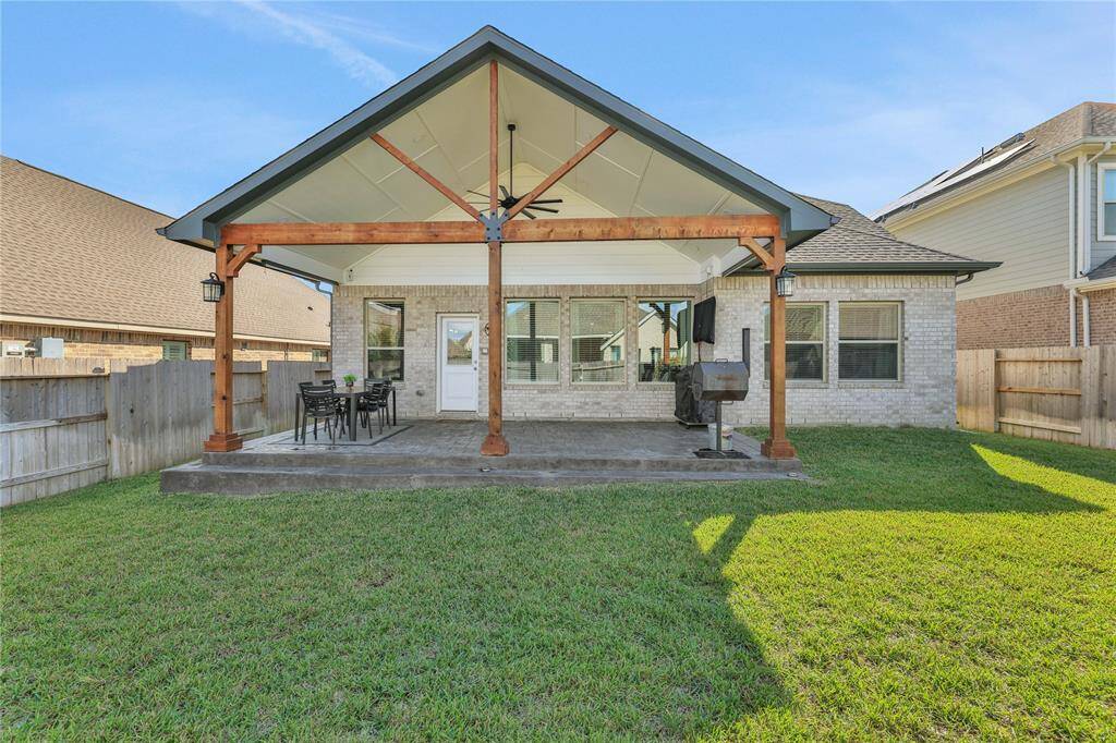 This is a spacious backyard featuring a large covered patio with a modern open-beam design, ideal for outdoor dining and relaxation. The yard is well-maintained with a lush green lawn, and the area is enclosed by a wooden privacy fence.