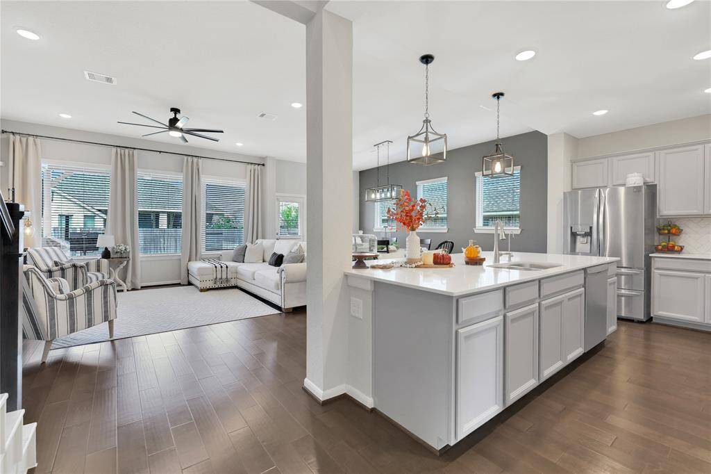 This is a modern, open-concept living space featuring a spacious kitchen with a large island and stainless steel appliances, leading into a cozy living area with ample natural light. The elegant design includes neutral colors and hardwood floors, creating a welcoming environment for entertaining and relaxation.