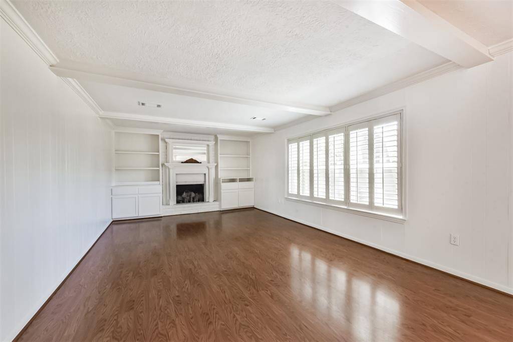 The den showcases laminate floors, crown molding, fireplace, plantation shutters and built-ins.