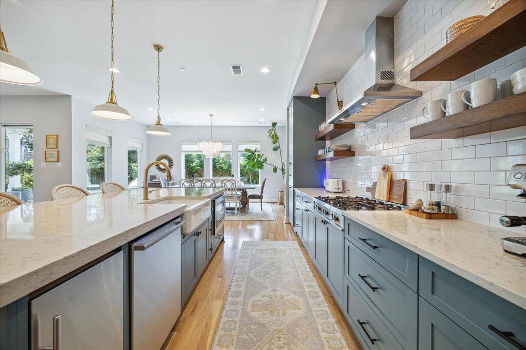 Premier stainless steel appliances include: a 5-burner, Bertazzoni gas range with wall-mount range hood above, and at the island, a Bosch dishwasher, Whirlpool microwave oven, ice maker, and a Kohler farmhouse sink.