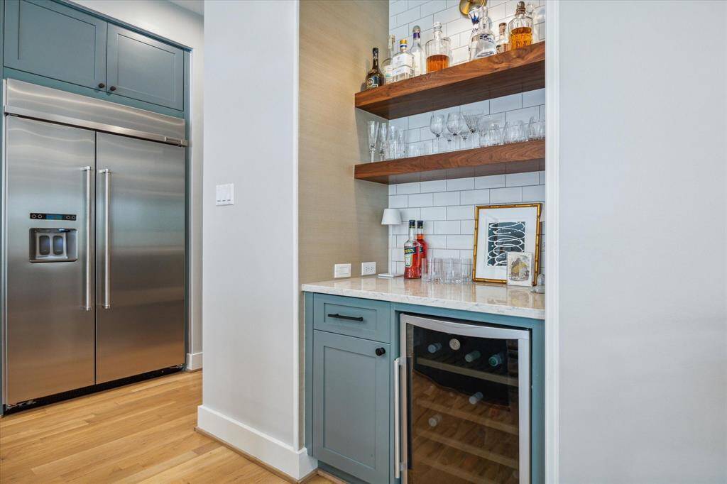 Perfect for entertaining, the convenient built-in bar is complete with a sleek Silestone countertop, subway tile backsplash, Philip Jeffries grasscloth wallpaper, floating shelves, sconce lighting, and a GE wine refrigerator.