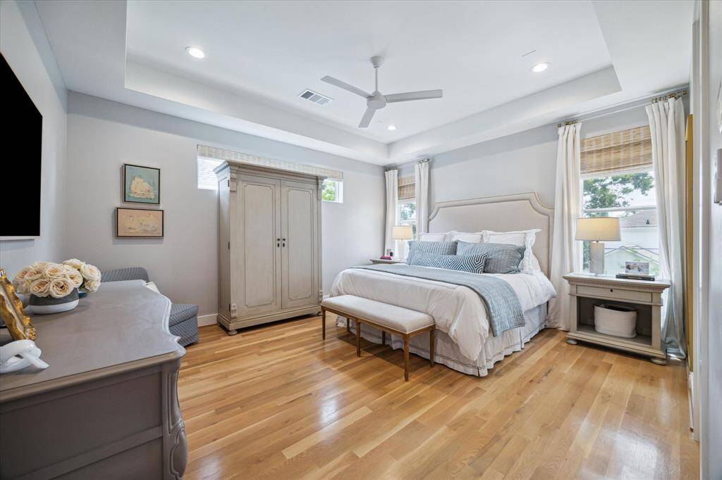 The beautiful primary bedroom boasts a 10-foot tray ceiling with recessed lighting and a modern triple-blade ceiling fan, creating an airy and elegant atmosphere. Hardwood flooring and automated window shades add to the luxurious feel, while the spacious layout provides ample room for a cozy sitting area, making it a perfect retreat within your home.