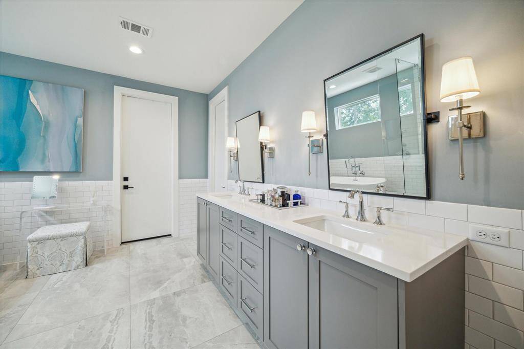 The luxurious primary bath showcases double sinks with sleek Silestone countertops, ample cabinet storage, elegant sconce lighting, and oversized tile flooring. To the right, a door leads to the private water closet, while straight ahead lies the expansive walk-in closet, offering generous storage space and convenience.