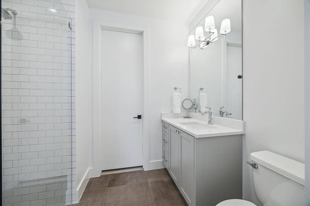 The ensuite bath has tile flooring, Silestone countertops, an updated, mirror-mounted light fixture, and a glass-enclosed walk-in shower with subway tile surround. Door opens to a spacious walk-in closet.