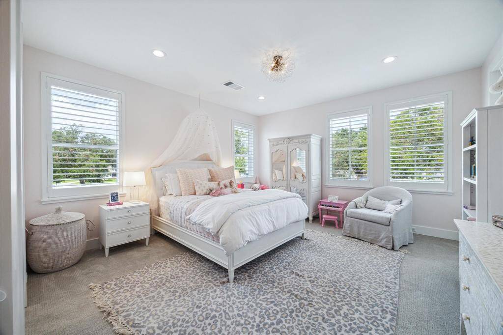 Surrounded by windows with shutters, this precious bedroom features a flush mount crystal light fixture from Restoration Hardware, recessed lighting, carpet flooring and walk-in closet.