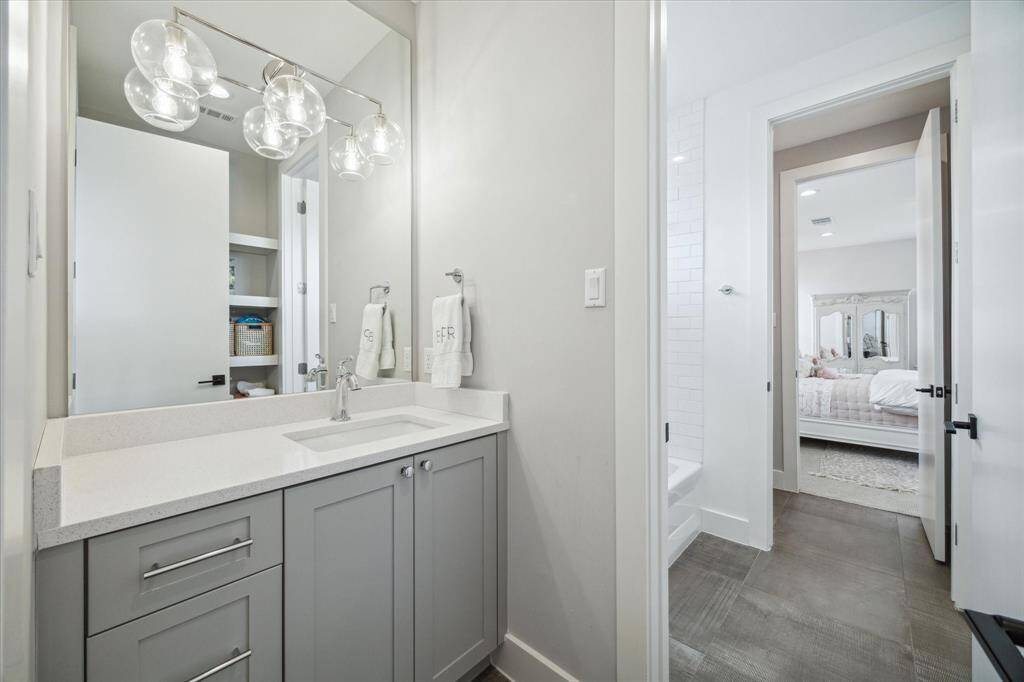 The shared bath for Bedrooms #3 and #4 features private sinks, tub/shower combination with subway tile surround, tile flooring and open shelving for linens and storage on each side.