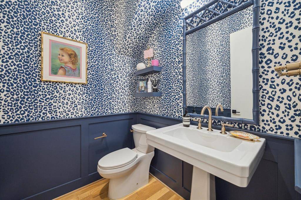 The adorable powder room is lined by Schumacher's Iconic Leopard wallpaper, with deep blue wainscoting, and brass hardware.