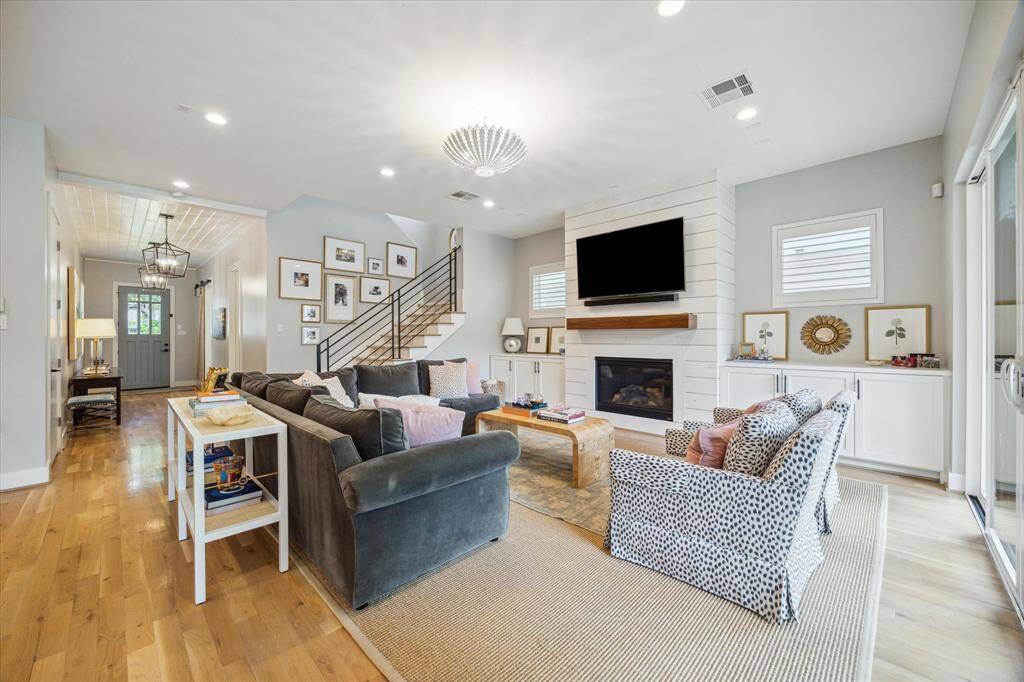 Blonde hardwood flooring continues into the open family room, which features a striking floor-to-ceiling shiplap accent wall, a gas-log fireplace, and a wooden mantle. Flanking the fireplace are built-in storage cabinets, with shuttered windows above.
