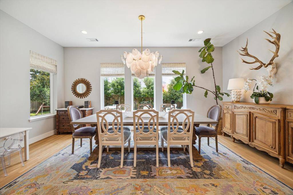 The spacious dining room offers ample space for entertaining and is surrounded by windows with automated shades, providing beautiful views over the backyard. [note: this light fixture has been replaced with a linear chandelier (Aug 2024)]