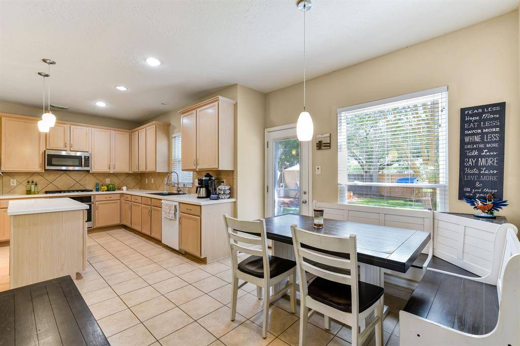 The kitchen is light and bright, featuring light wood-look cabinetry that adds warmth, paired with smooth hard surface  countertops for a sleek, modern touch. Abundant natural light fills the spaceThe breakfast area provides a cozy spot for casual dining, making this kitchen a perfect blend of style and functionality.