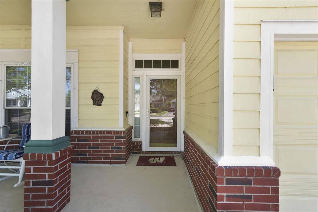 Welcoming front door entryway with a classic Southern touch. The front door is accented with a full-length glass storm door and a transom window above, allowing for extra natural light to filter into the interior. To the left, there’s a cozy sitting area perfect for relaxing and enjoying the front yard.