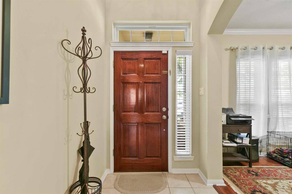 This photo captures a warm and welcoming entryway featuring a rich, wooden front door with a transom window above and a tall sidelight window to the right, allowing natural light to brighten the space.