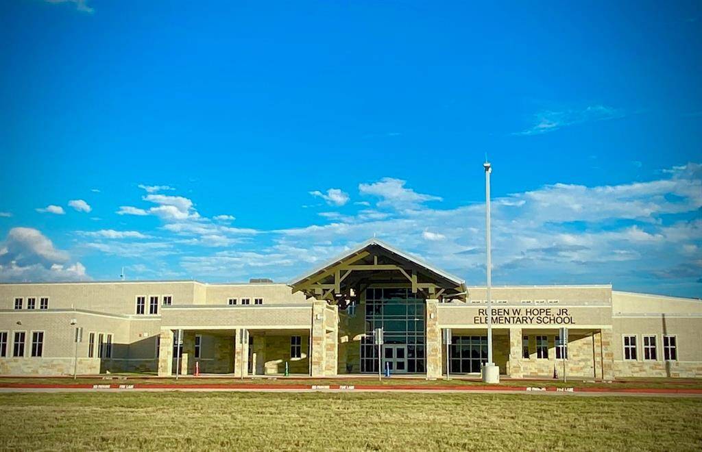 In neighborhood modern elementary school building with a large entrance and a flagpole in front, set against a clear blue sky. The area appears well-maintained, suggesting a family-friendly neighborhood and convenience for early education years