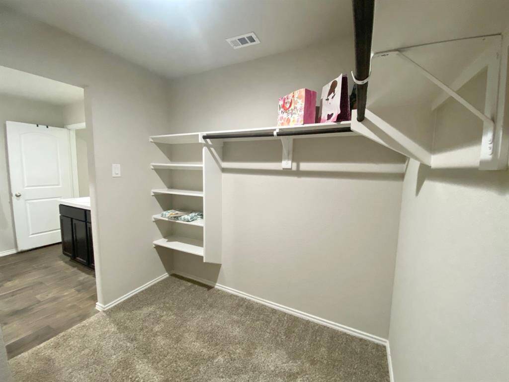 Spacious walk-in closet with built-in shelves and a hanging rod. It features carpeted flooring and leads into your private retreat.  Ideal for organized storage and easy access.