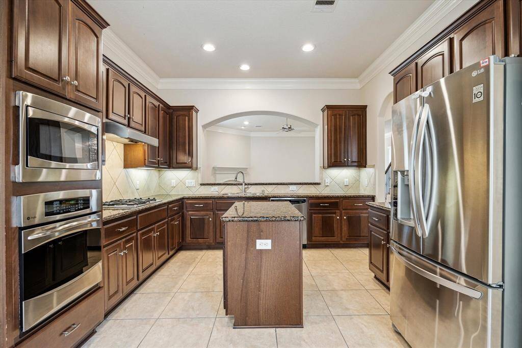 The gorgeous gourmet kitchen features rich dark wood cabinetry, providing ample storage space, complemented by high ceilings with recessed lighting for a bright and open feel. A conveniently placed wet bar overlooks the main living area, enhancing connectivity and flow—perfect for entertaining.