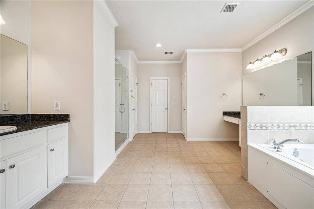 The primary bath retreat exudes spa-like luxury, featuring a soaking tub, dual vanities, a spacious glass-enclosed standing shower, and direct access to separate his-and-hers walk-in closets for ultimate comfort and convenience.