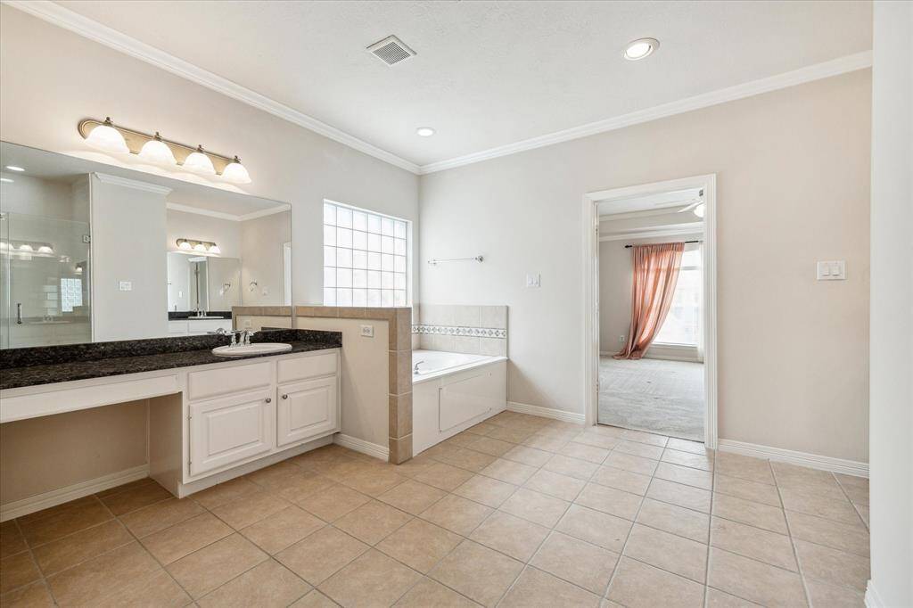 The primary bath showcases Jack-and-Jill vanities with overhead lighting, expansive mirrors, generous counter space, and ample cabinet storage. A luxurious spa-like soaking tub offers the perfect retreat for relaxation, while frosted windows allow abundant natural light to fill the space while maintaining privacy.