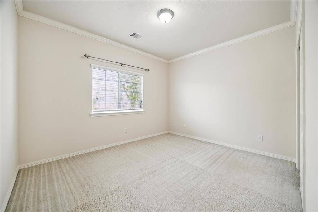 The third bedroom on the second level features high ceilings with elegant crown molding, a soothing neutral palette, and lovely views of the backyard. It also includes its own closet and convenient access to a shared bath, combining comfort with practicality.