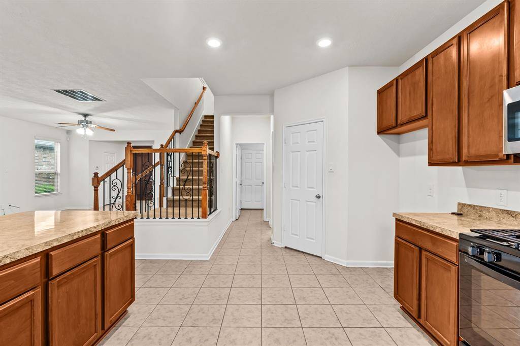 A utility room with tile flooring, white walls, and built-in shelving. It has hookups for a washer and dryer, and there's a view into a kitchen area