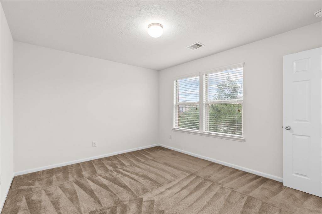 Bright, spacious bedroom with neutral carpet, large windows for natural light, and a walk-in closet.