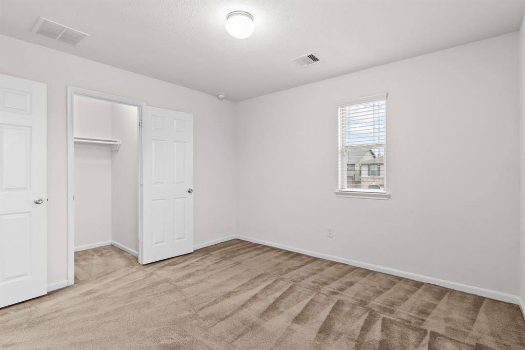 This room features neutral walls, carpeted flooring, and bright lighting. It includes a closet with double doors, offering ample storage space. Ideal for a bedroom or home office.