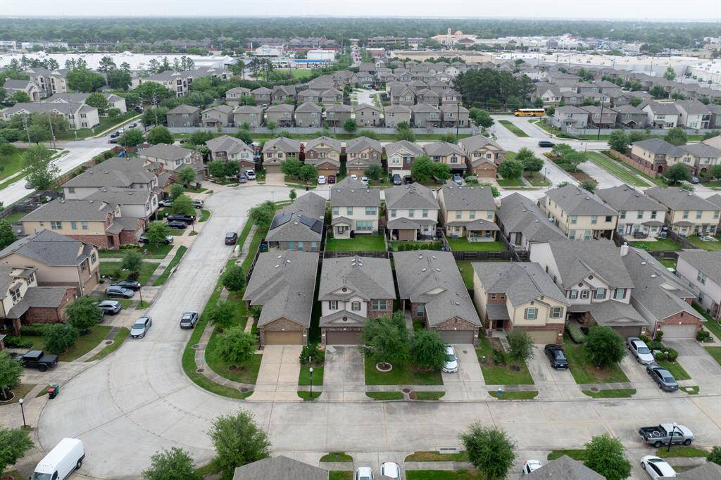 This aerial photo showcases a suburban neighborhood with well-maintained, two-story homes on a quiet cul-de-sac. The area is lush with greenery and features ample street parking. In the background, commercial areas and additional housing are visible, indicating a convenient location with nearby amenities.