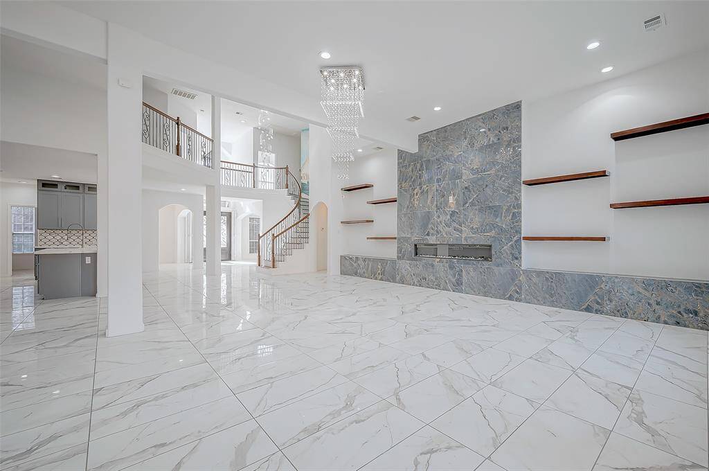 Family Room: The remodeled open-concept family room adds 500 sq ft, features marble tile surrounding an electric fireplace, built-in custom wood shelving, and motorized blinds.