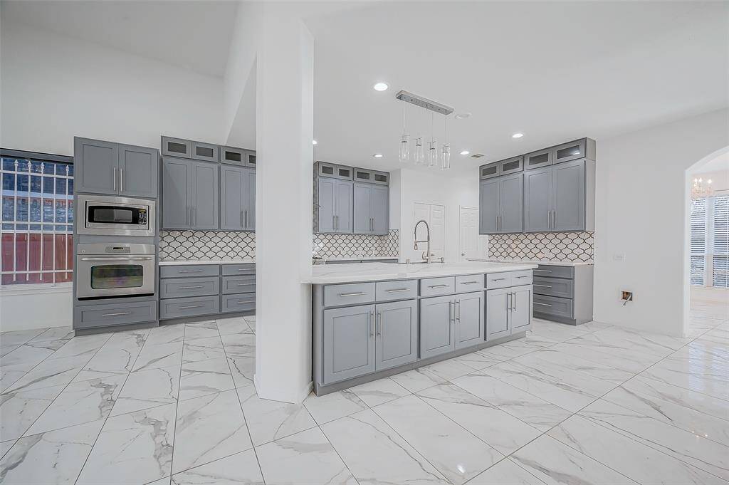 Gourmet Kitchen: Large center island with a drop-down farm sink and overhanging pendant lights. Abundant cabinetry with brushed nickel hardware, extending to the ceiling with display cabinets at the top. Stainless steel appliances, including a six-burner gas stove with a stainless-steel hood. Beautiful tile backsplash and additional storage in the kitchen island.