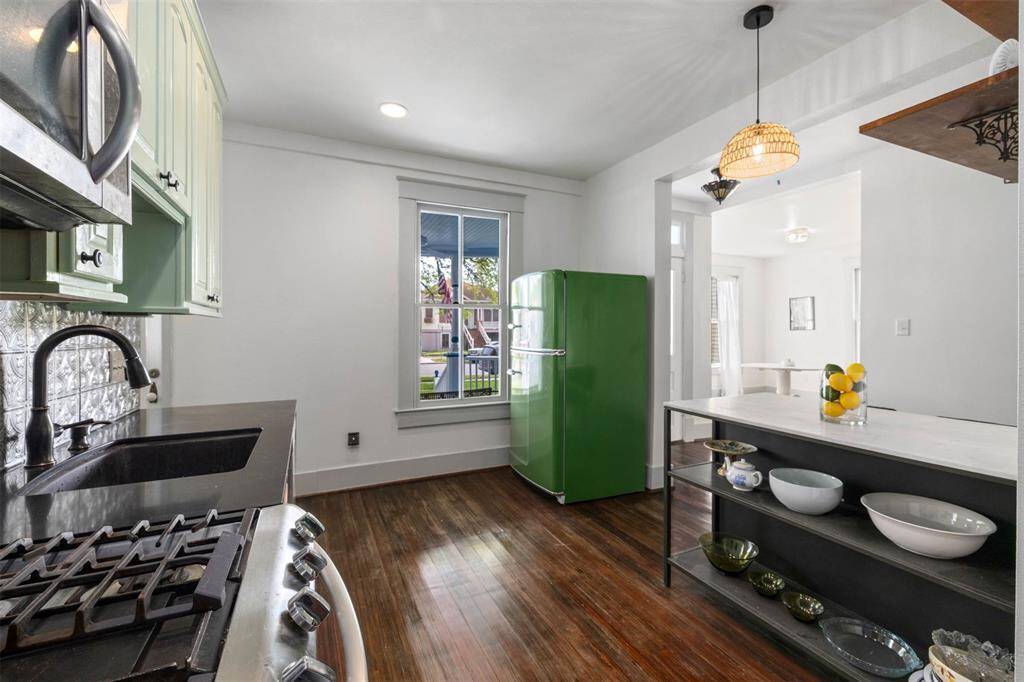 This kitchen features a vintage-inspired green refrigerator, sleek black appliances, and a stylish island with open shelving. The space is bright with natural light from a window, and it has a blend of modern and retro elements.
