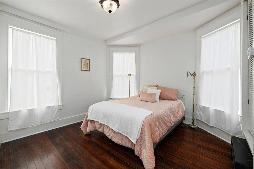 Bright and cozy downstairs bedroom with hardwood floors, large windows with sheer curtains, and a simple yet elegant decor.