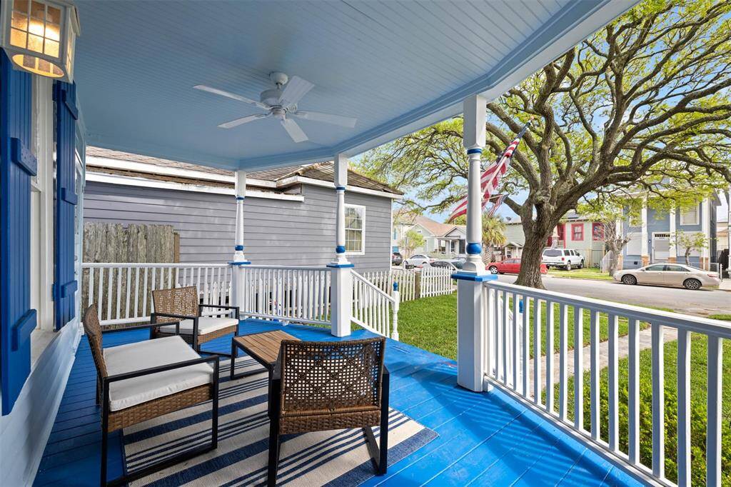 Charming front porch with a vibrant blue floor and ceiling, featuring cozy seating and a ceiling fan. It overlooks a quiet neighborhood street with mature trees, providing a relaxing outdoor space.