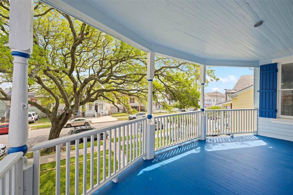 This photo showcases upstairs covered porch with vibrant blue flooring and ceiling, offering a peaceful view of a tree-lined street. Ideal for relaxing and enjoying the neighborhood atmosphere.