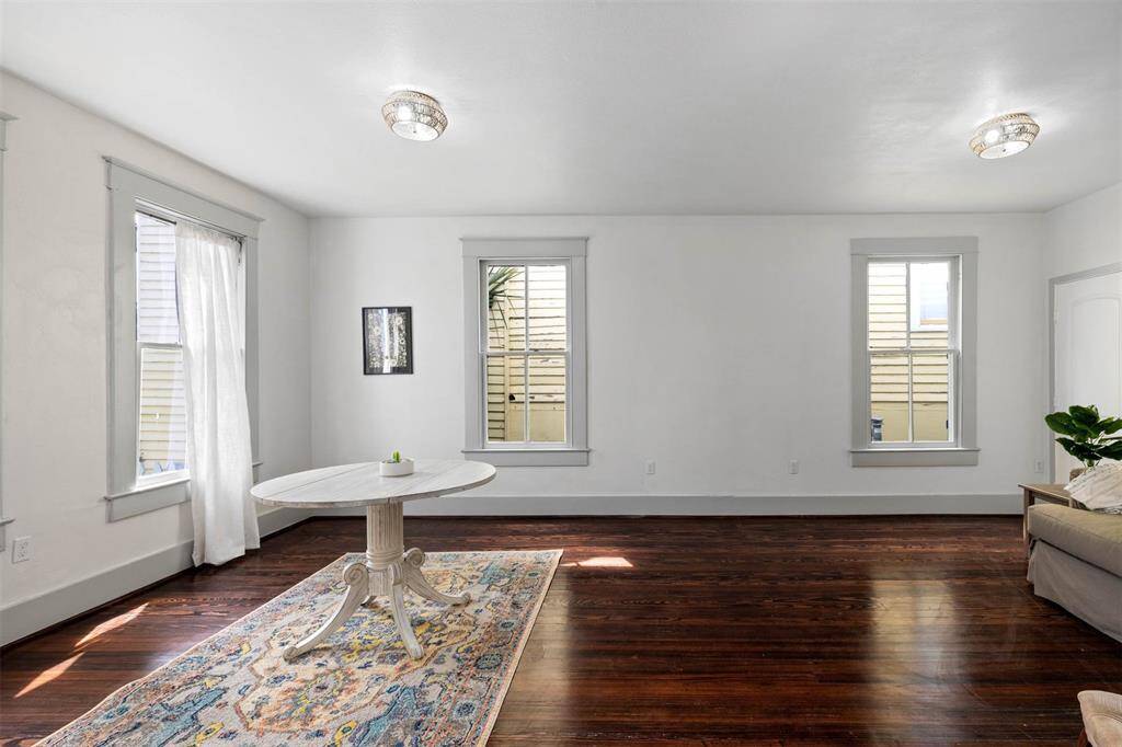 This bright, spacious room features dark hardwood floors, white walls, and ample natural light from multiple windows.