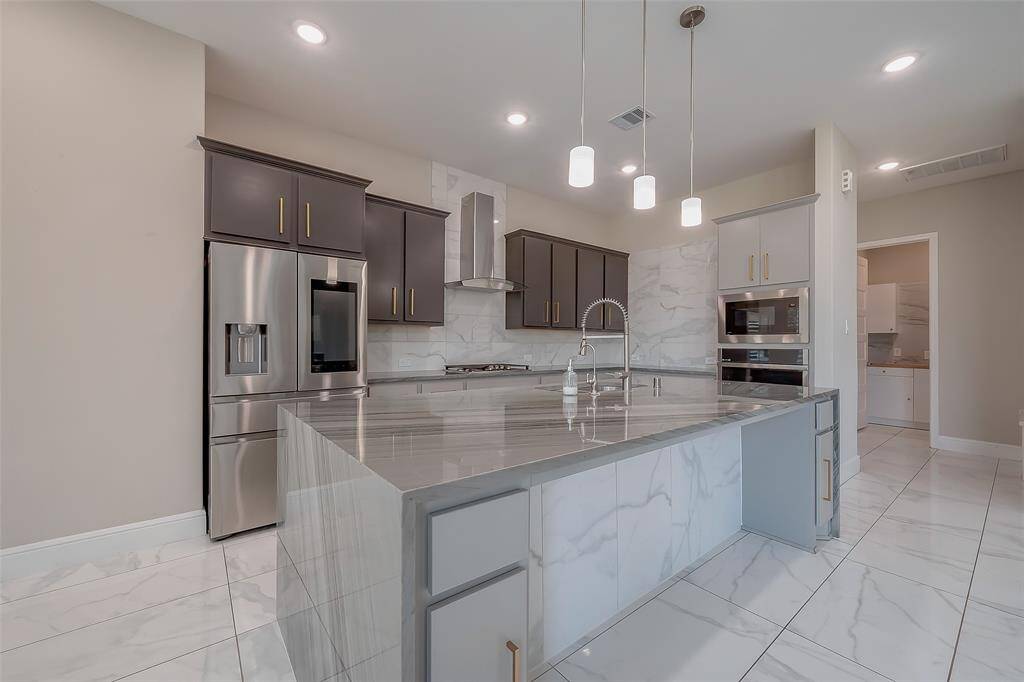 The kitchen is a chef’s dream, designed with Quartz countertops, a large island featuring built-in storage and seating, and overhanging pendant lighting. The open concept allows for a seamless flow into the breakfast area and family room. Unused stainless steel built-in appliances, a hooded gas range, and a fabulous tile backsplash create a stylish yet functional cooking space.