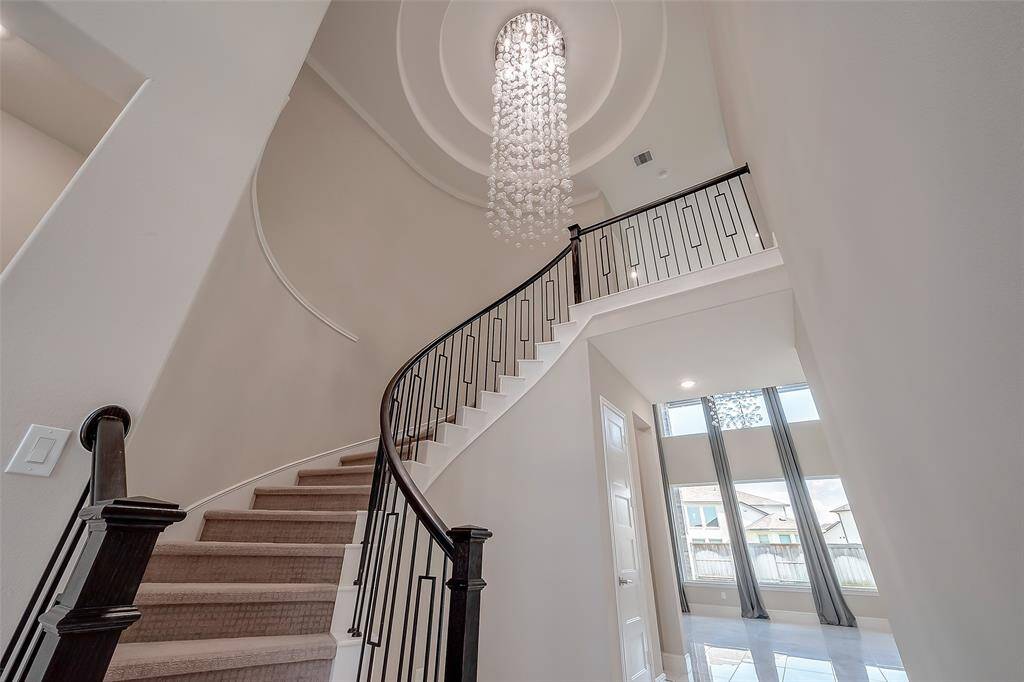 The curved staircase with wrought iron spindles and balcony overlook sets the tone for elegance. A stunning rotunda ceiling above the stairwell, crowned with a dazzling modern chandelier, draws the eye upward and sets the home’s sophisticated aesthetic.