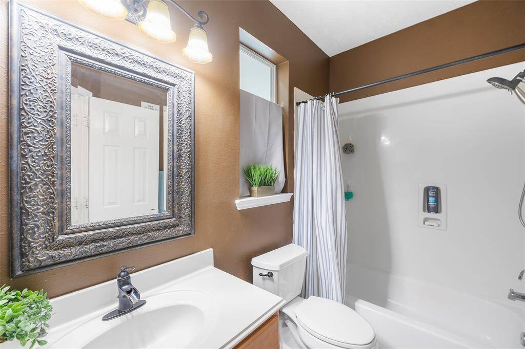 Secondary bath features tile flooring, bath/shower combo with tile surround, stained wood cabinets, beautiful light countertop.