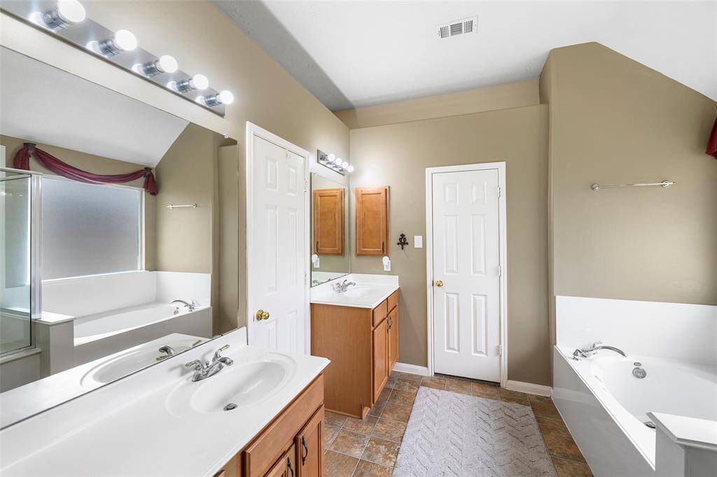 Spacious primary bathroom featuring dual vanities, a soaking tub, separate walk-in shower, and ample cabinet storage.