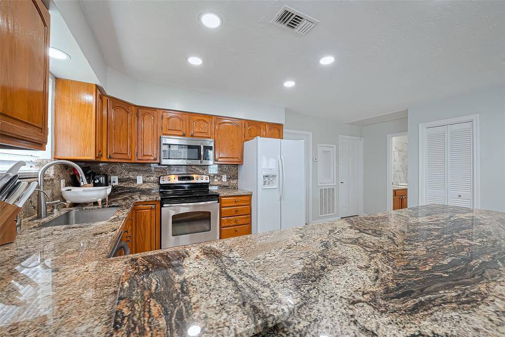 Modern kitchen featuring granite countertops, stainless steel appliances, and warm wooden cabinetry. Bright lighting and ample space enhance functionality.