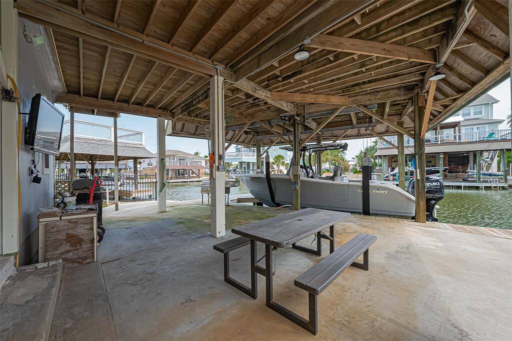 This covered dock area features a boat slip with a lift, a picnic table, and a TV, perfect for waterside relaxation and entertainment. The setting is ideal for boating enthusiasts with easy access to the water.