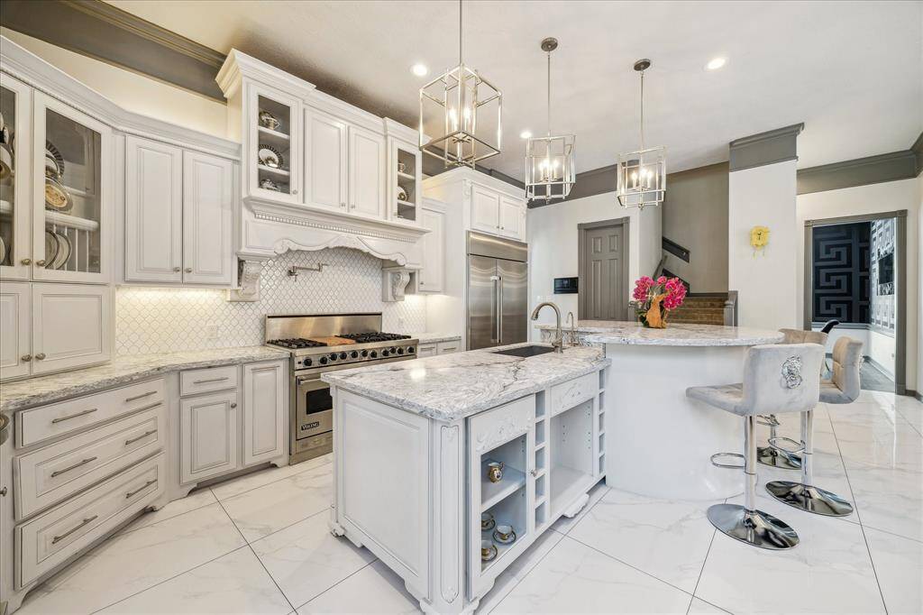 This kitchen features elegant white cabinetry, a large island with seating, stainless steel appliances, and modern pendant lighting, creating a bright and stylish culinary space.